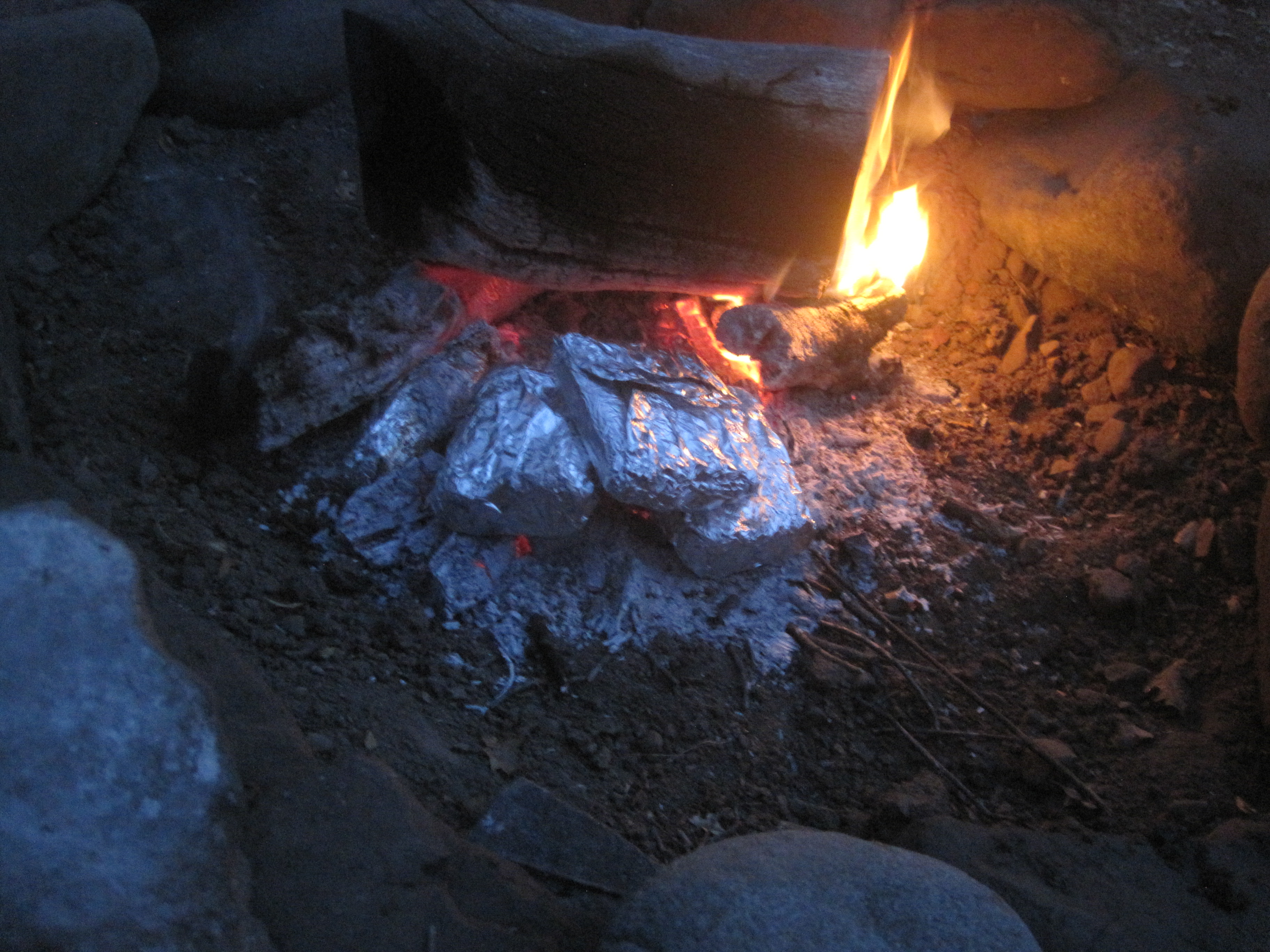 Corn and sausages cooked in tin foil over a fire.
